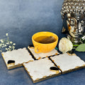 A set of white marble agate coasters with gold foiling on the edges, displayed on a table with a cup of tea and a decorative buddha statue in the background.