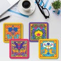 A set of four colorful square coasters with a pearl white glitter finish, displayed on a table alongside a cup of coffee, glasses, and some papers.